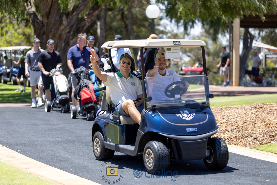 Two male golfers seated in a gold cart, one is waving to the camera